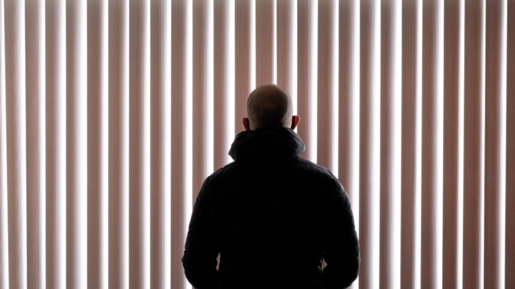 A man standing in front of window shades from behind