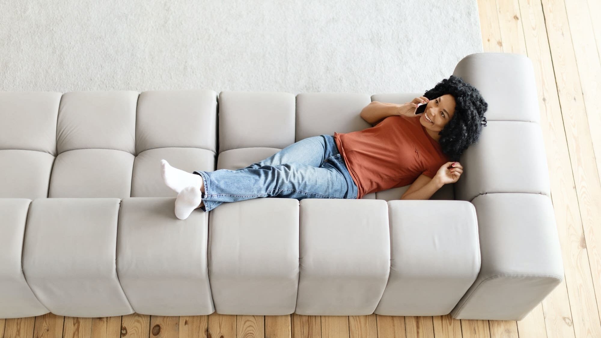 Happy Black Woman Talking On Cellphone While Lying On Couch At Home