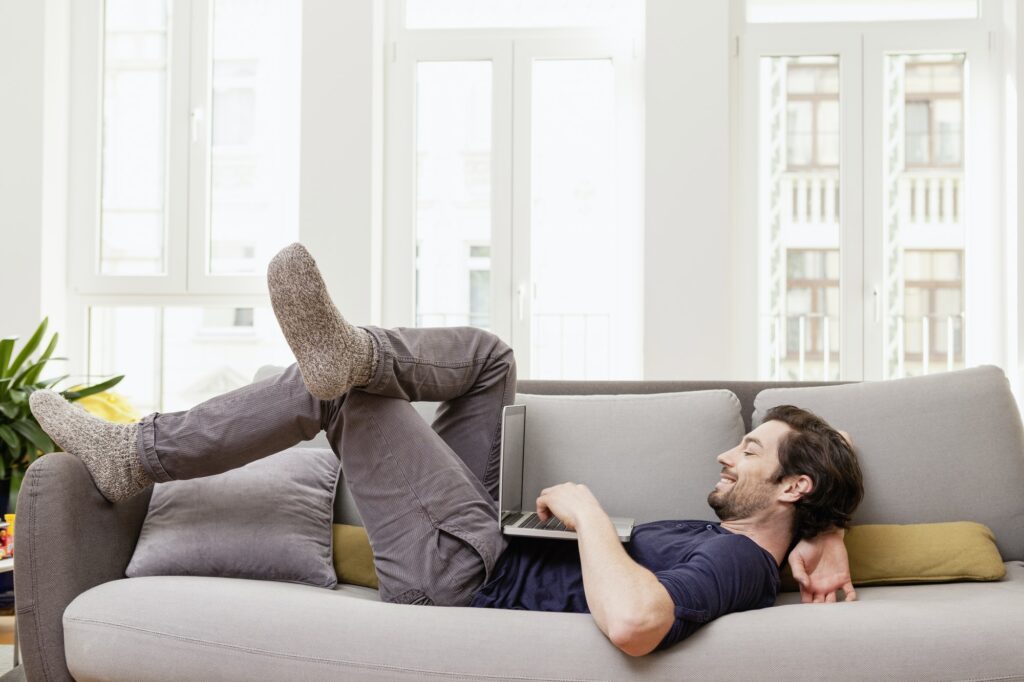 Relaxed man lying on couch using laptop with enhance privacy and comfort with automated shades