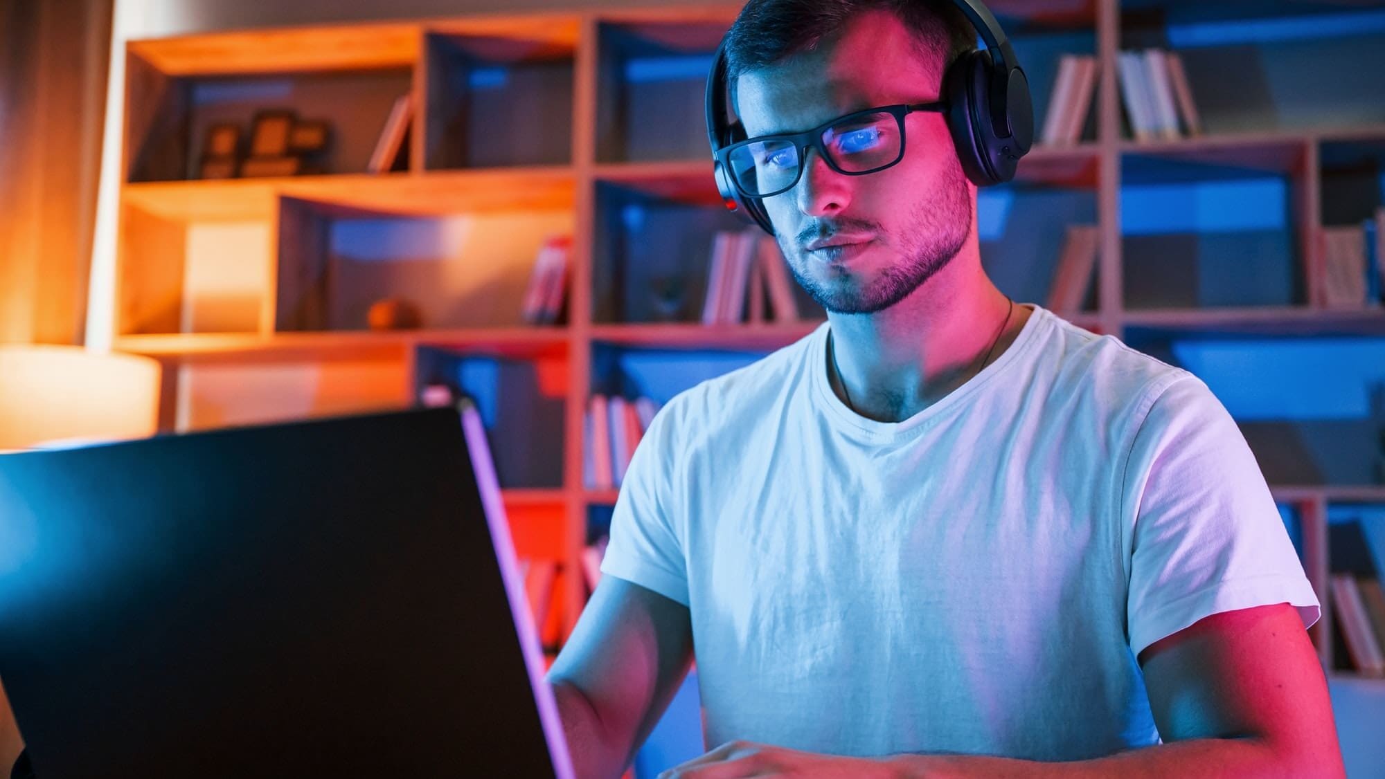 Man in glasses and white shirt is sitting by the laptop in dark room with neon lighting with smart lighting and home automation integration