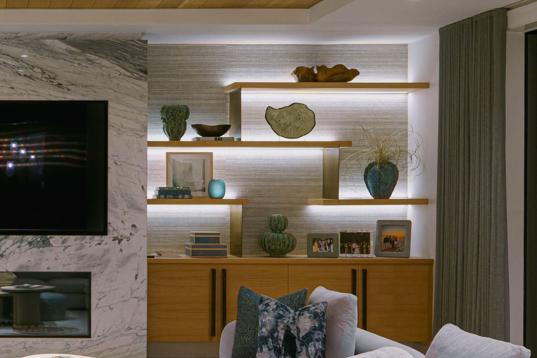 Detail of backlit floating shelves in warm oak beside a marble fireplace surround