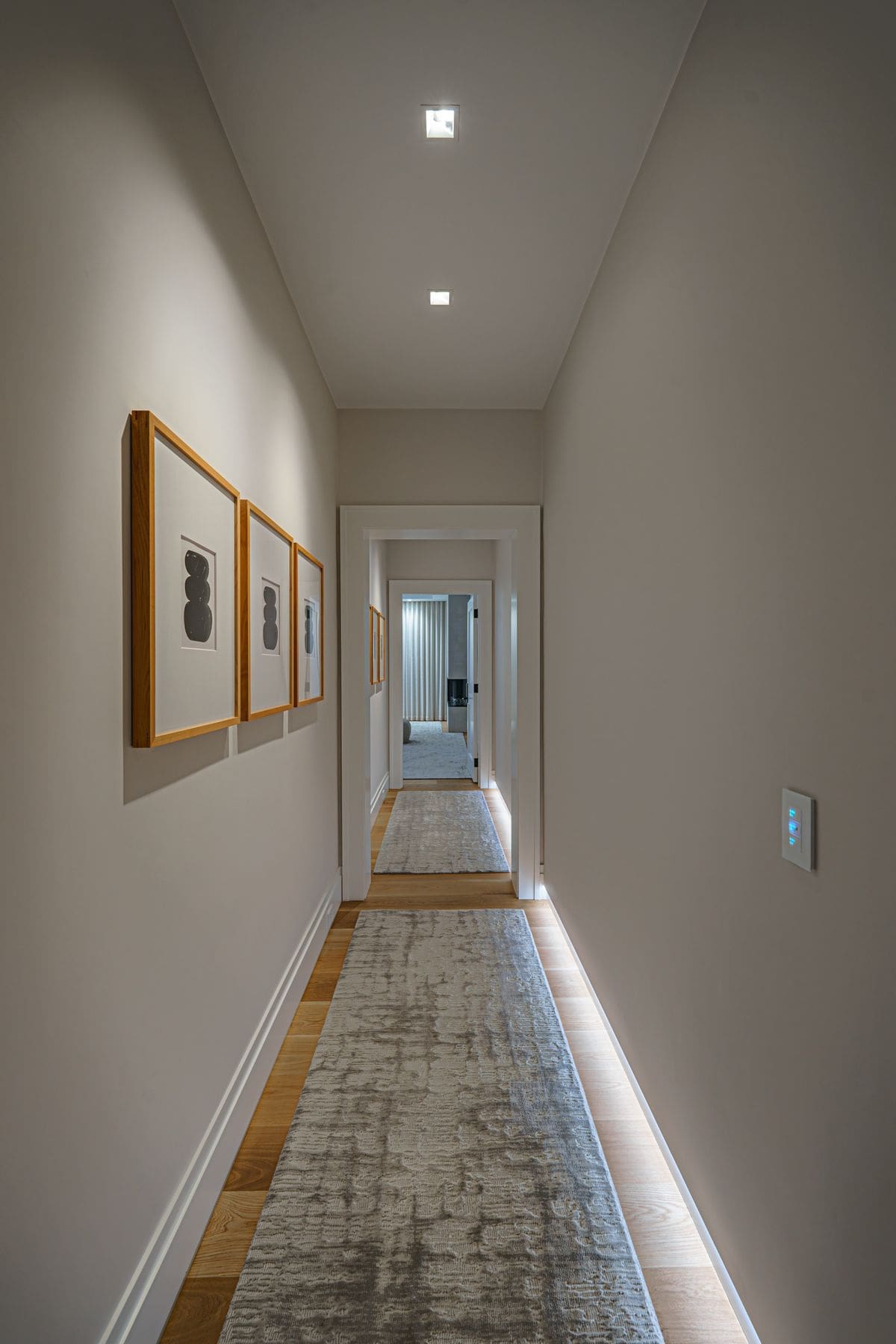 Gallery hallway with framed artwork, cove-lit runner and a flush-mounted keypad