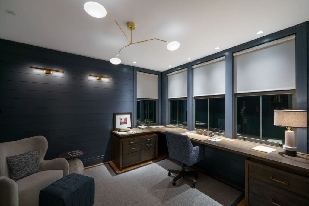 Home office with navy shiplap walls and Lutron Palladiom motorized roller shades on a window bank