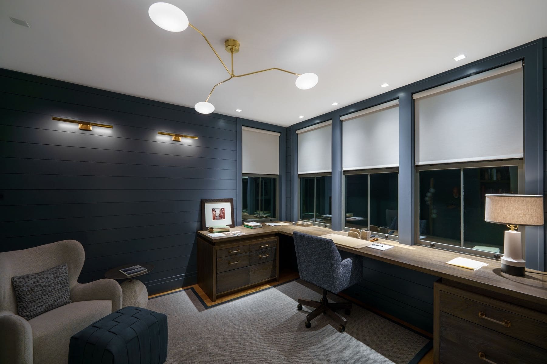 Home office with navy shiplap walls and Lutron Palladiom motorized roller shades on a window bank
