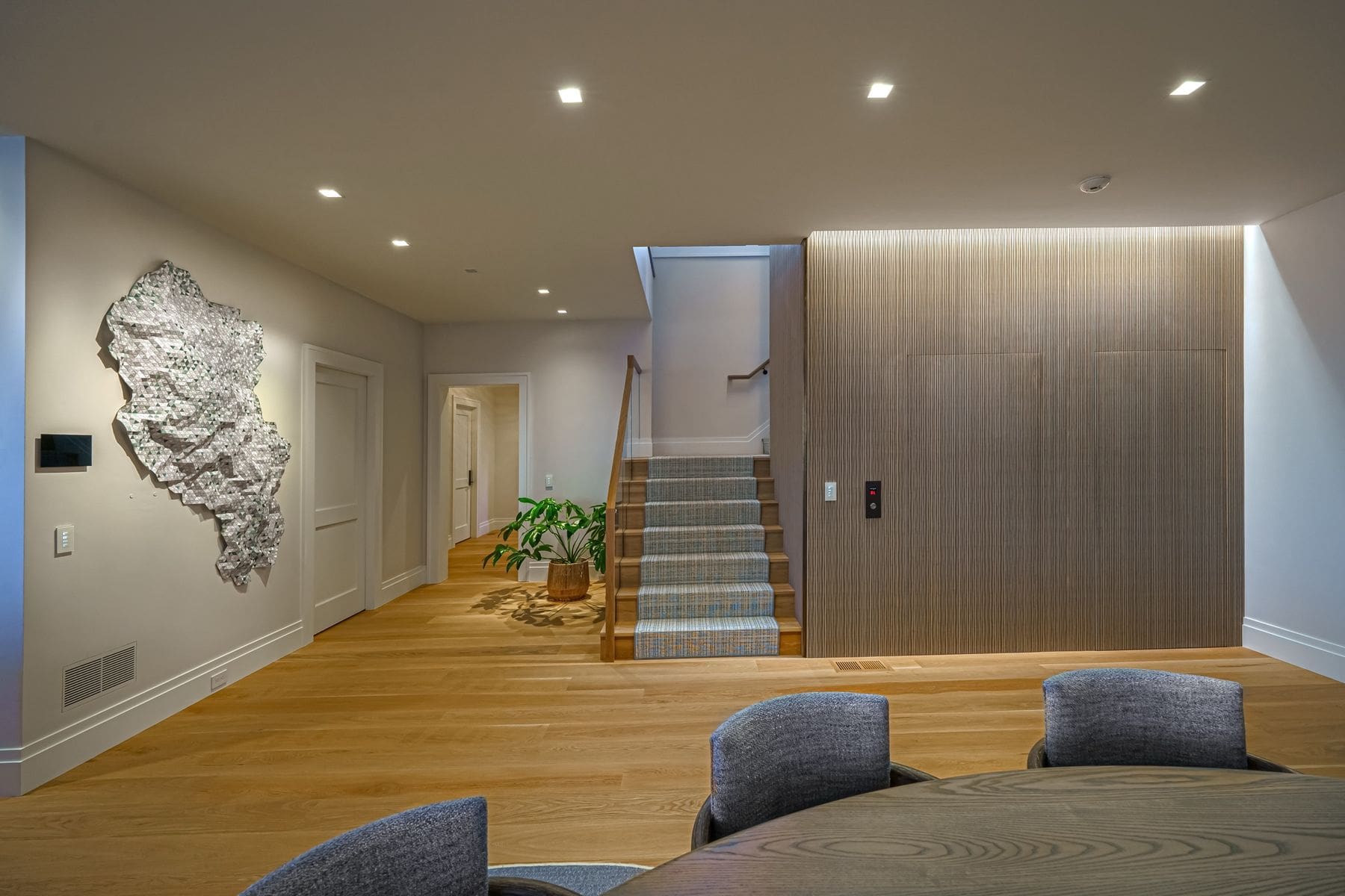 Lower level lounge with oak floors, sculptural wall art and a stair to the main level