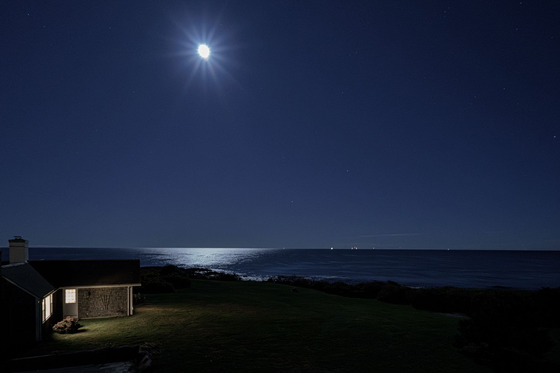 Oceanfront Narragansett home at night under a full moon with warm landscape lighting