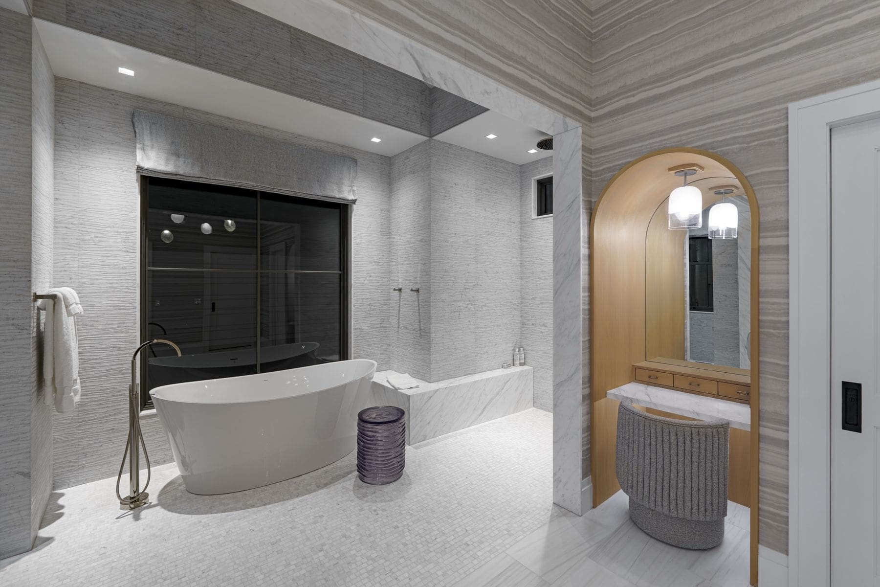 Primary bathroom in marble with freestanding tub, arched vanity alcove and tuned lighting