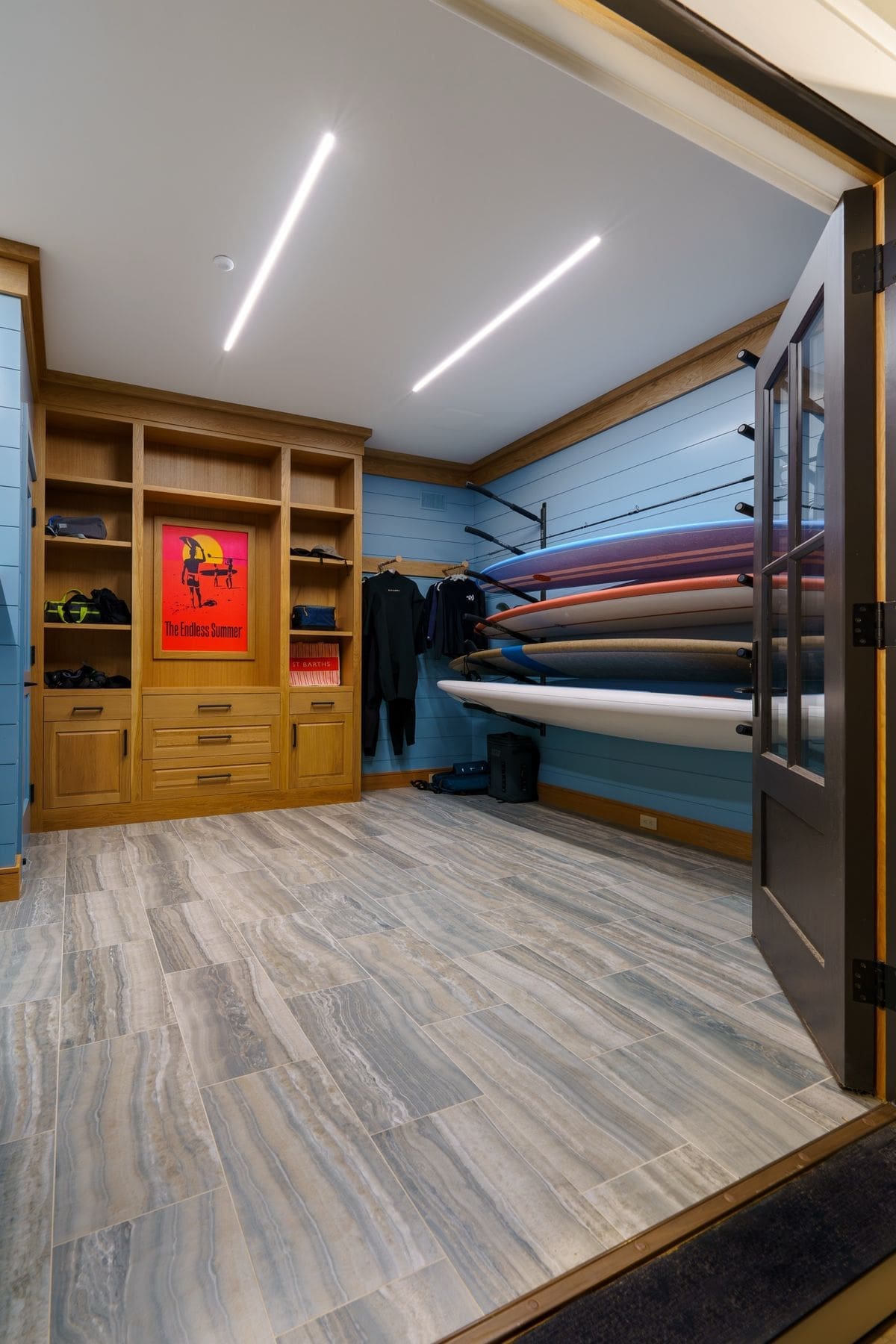 Custom surf and gear room with board racks, oak cabinetry and linear ceiling lighting
